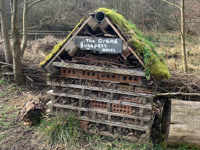 A bug hotel made of wooden palettes and bricks with a moss roof.