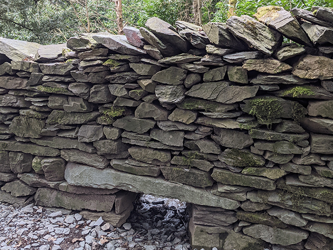 Dry stone wall with a small opening at ground level to allow water and wildlife to pass through.