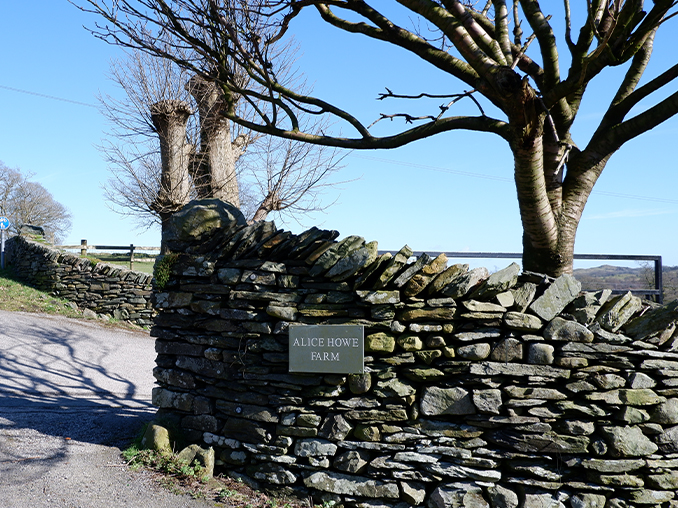 Dry stone wall at the entrance to a farm with a sign set into the wall.