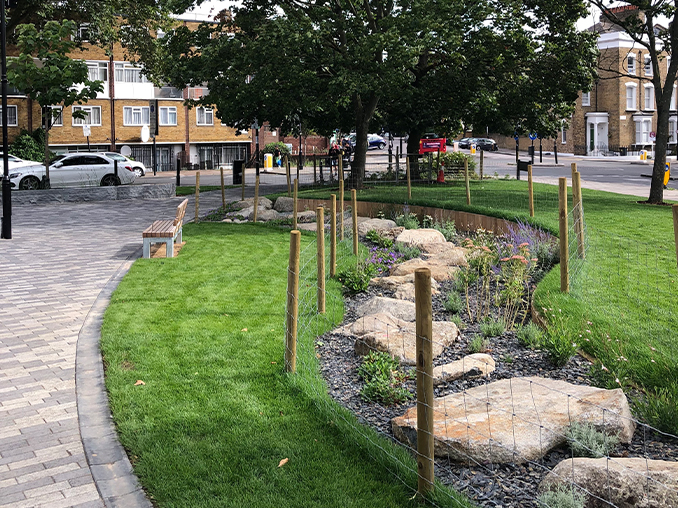 Large flat rocks amongst grass and tree planting next to a pathed walkway.