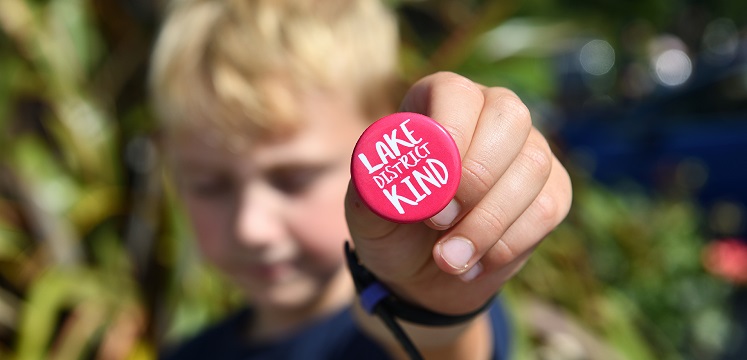 Child holding a Lake District Kind badge.