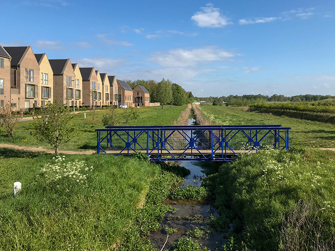 A bridge over a stream with the path leading to a housing estate.