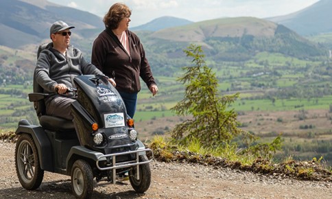 Photo of man on a tramper  with a woman walking by him, with hills in the background of the Lake District fells