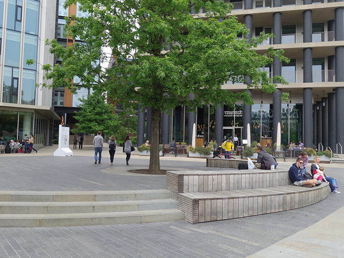 People sat on tiered seating around a tree outside a rail station.