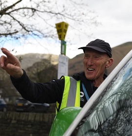 Volunteer smiling next to a visitors car.