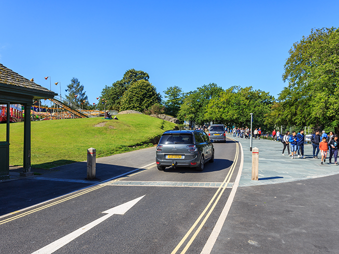 People walking on a wide pavement next to a one way road.