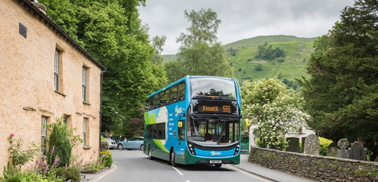 A blue bus with Keswick 555 displayed on a rual road