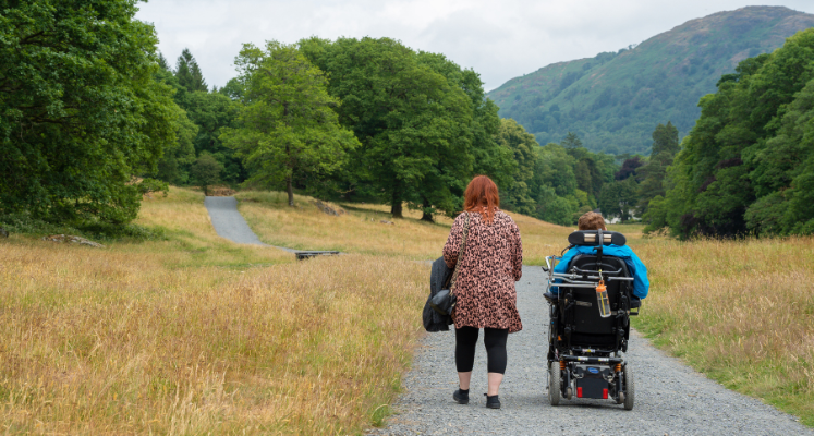 Woman walking next to man in wheelchair along a flat gravelled path