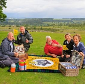 sitting on a picnic blanket is  David Bliss, Lowther Castle, Dylan Jackman, Ranger with Lake District National Park, Tim Clarke, Friends of the Ullswater Way, Suzy Hankin, Area Ranger with Lake District National Park and Anne Clarke, Friends of the Ullswater Way.