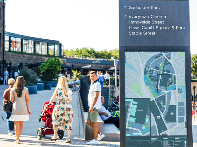 People walking past a large map and information board.