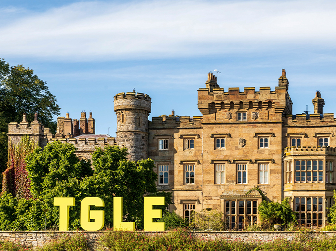 A historic stone manor house with large letters TGLE in front.