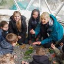 A group of children crouching on the ground with Learning and Engagement Manager Ruth Suddaby, as they listen to her intently