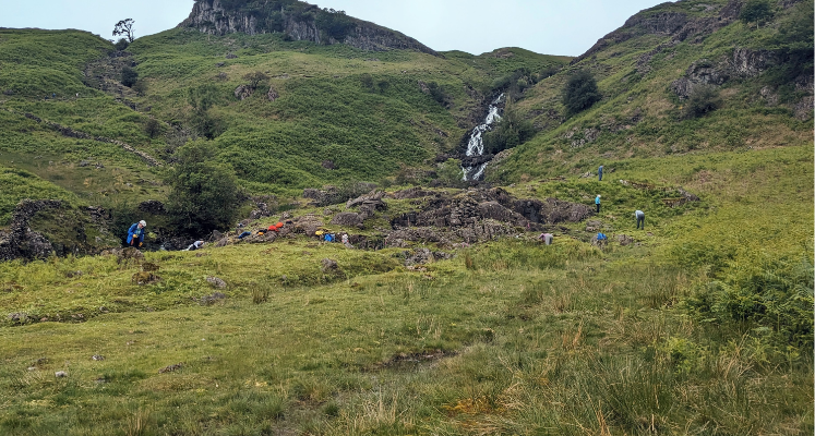Landscape shot of volunteers in the distance bracken bashing with waterfall backdrop