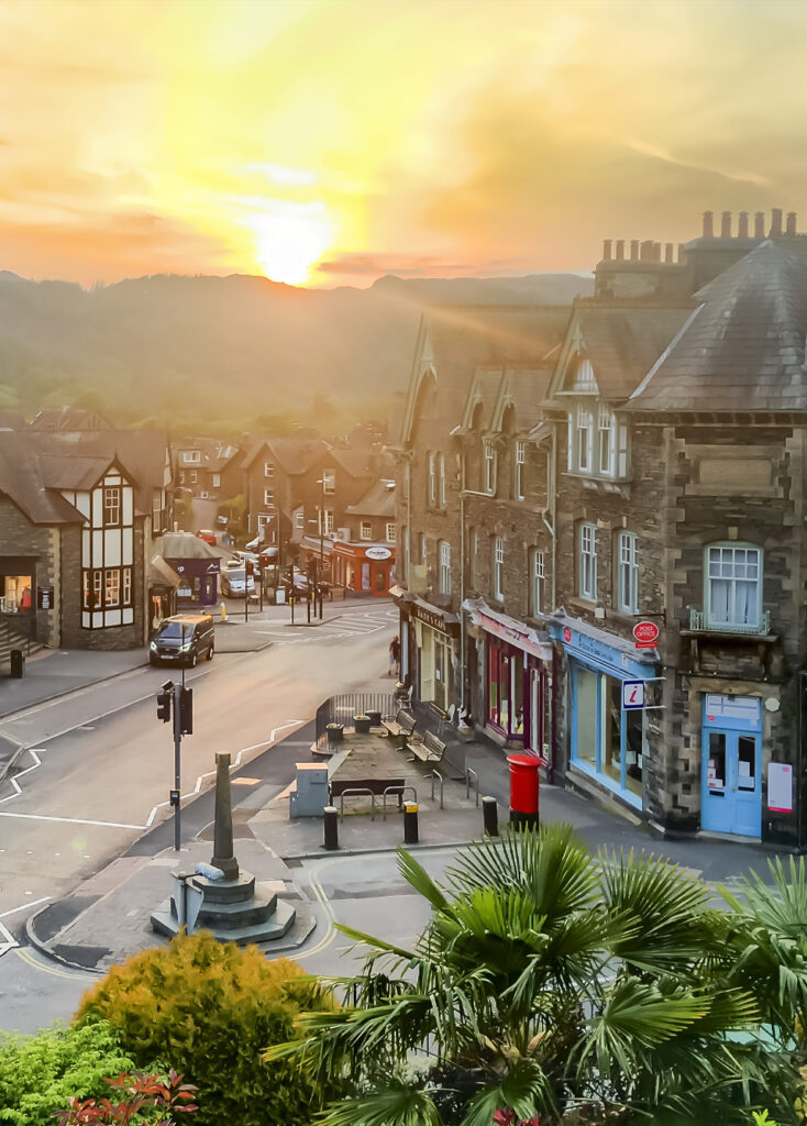 bright orange and yellow evening sunset lighting the distant fells and streets of Ambleside village, lined with shops, benches and bushes