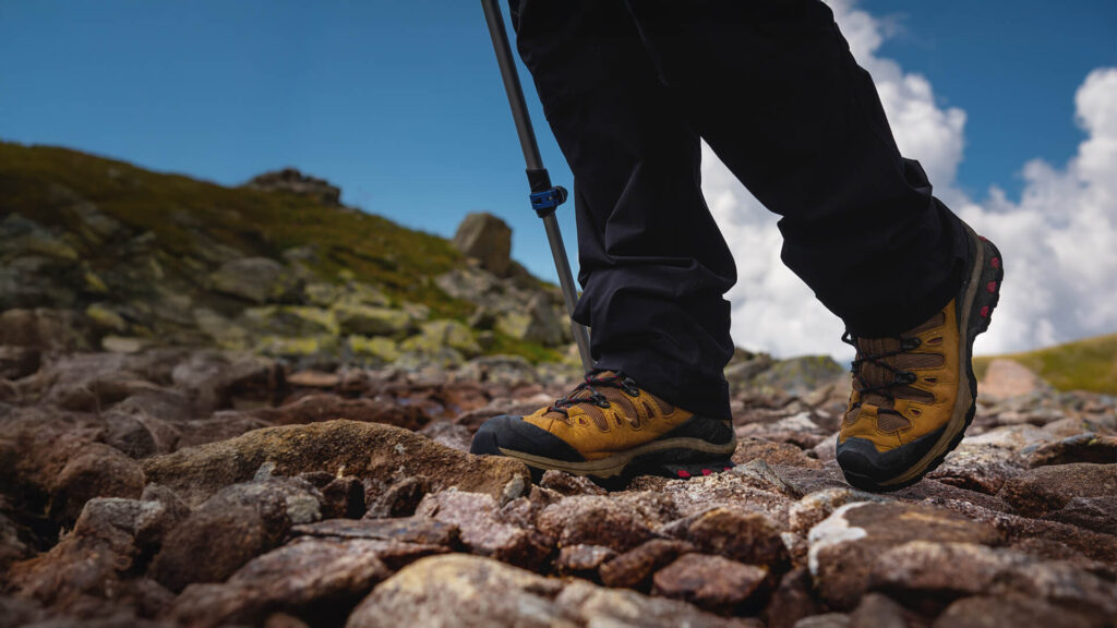 lower half of legs in walking gear and yellow walking boots on stone path next to shrub verge