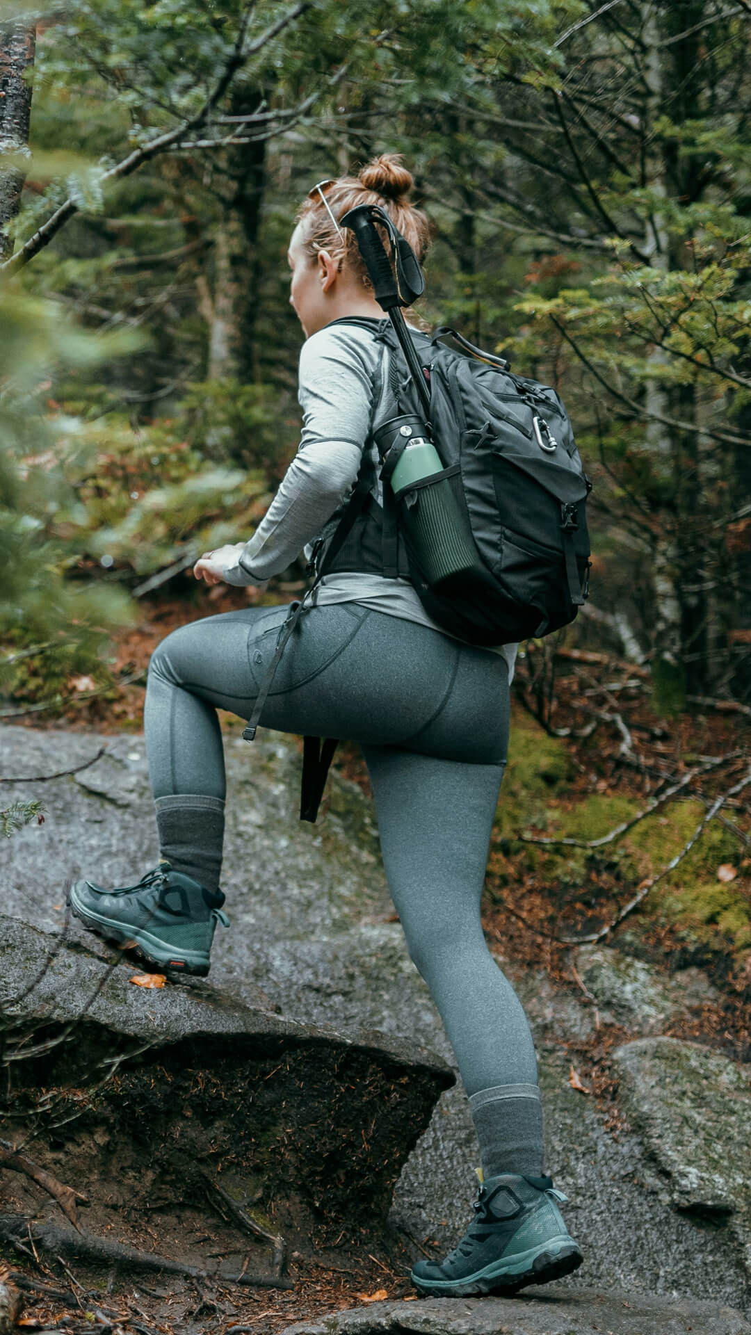 white adult female in grey walking clothing stepping on a stone path amongst dark green woodland