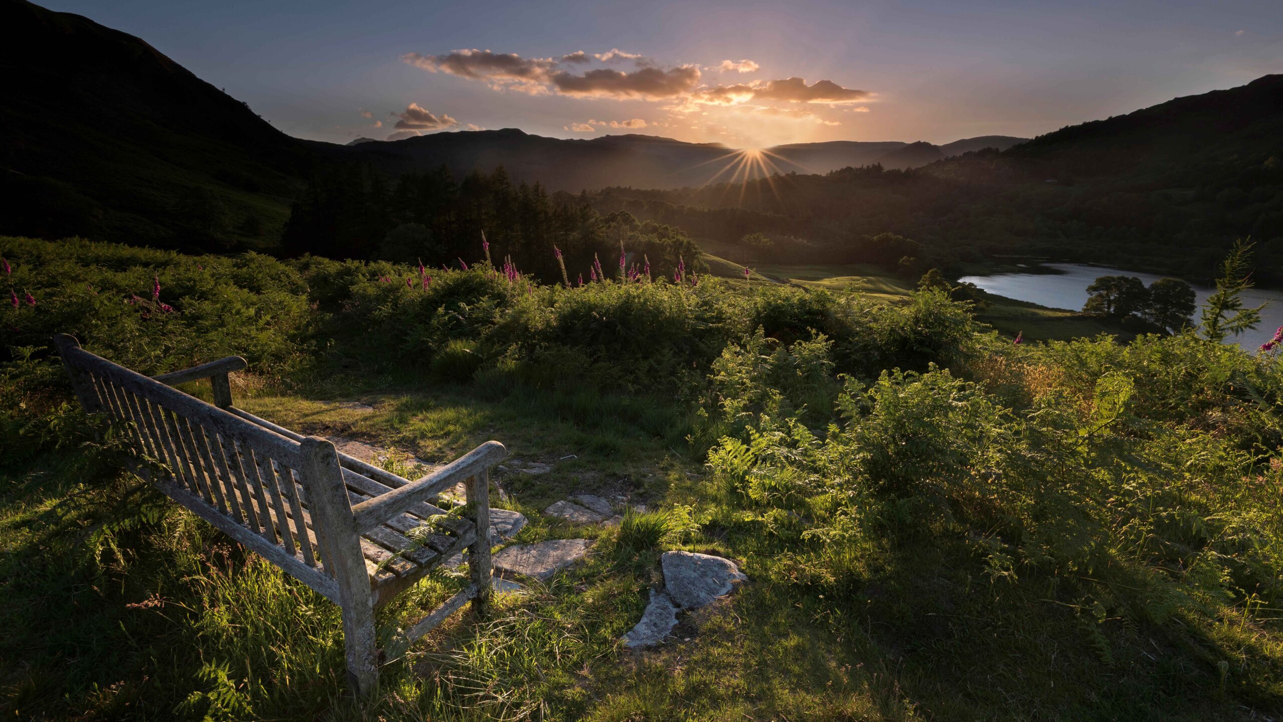 Bench on grass hill overlooking Grasmere and surrounding fells at sunset