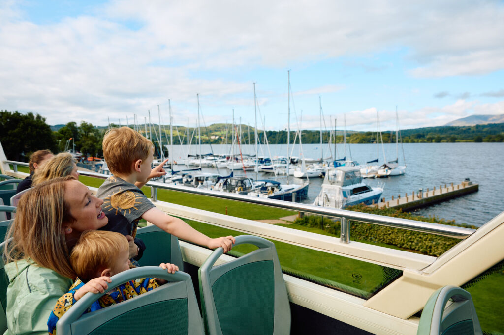 adult female and two young children sat on open top bus looking out to lake and moored boats