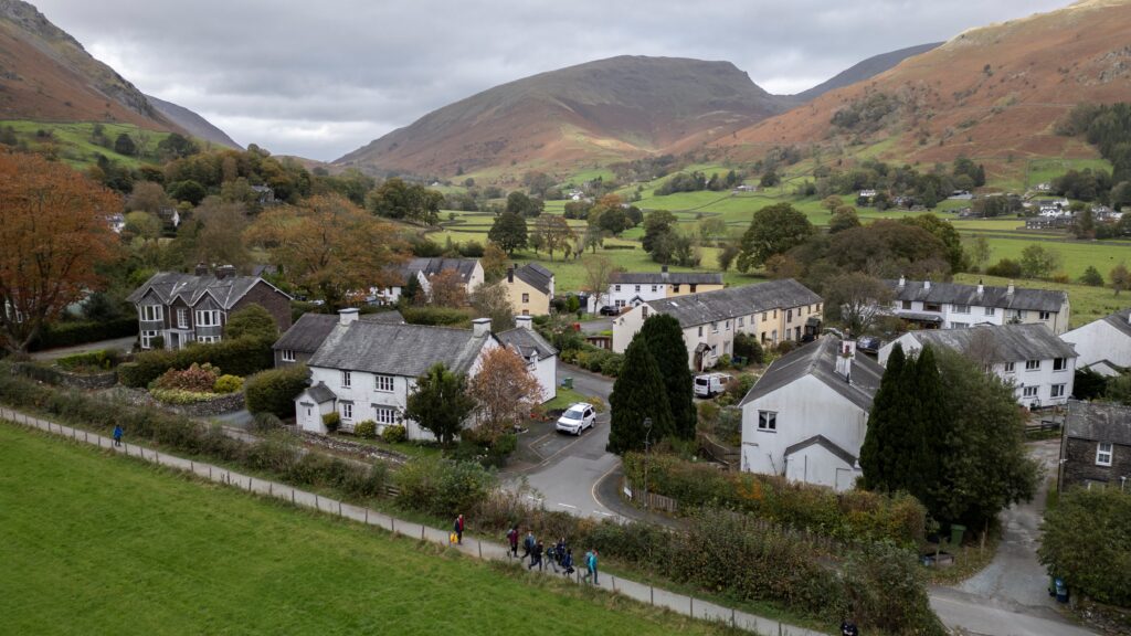 aerial view of rural village with white walled slate roof houses. village surrounded by green fields, woodland and low fells
