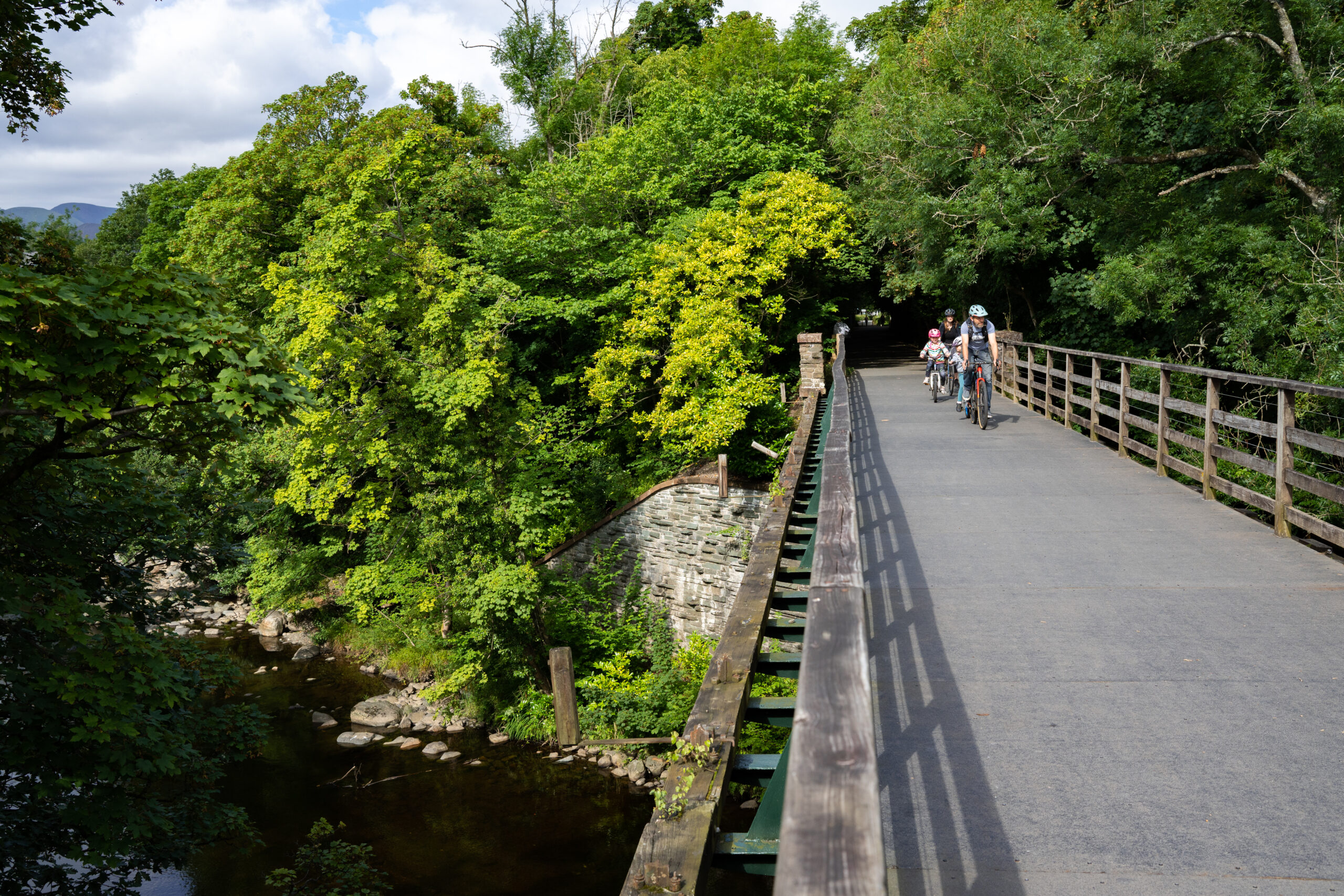 wide paved bridleway bright with two cyclists crossing surrounded by green woodland