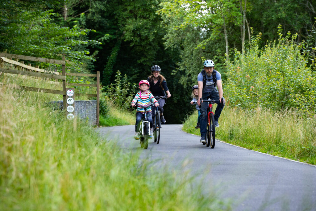 family cycling on a concrete path through green grasses and woodland