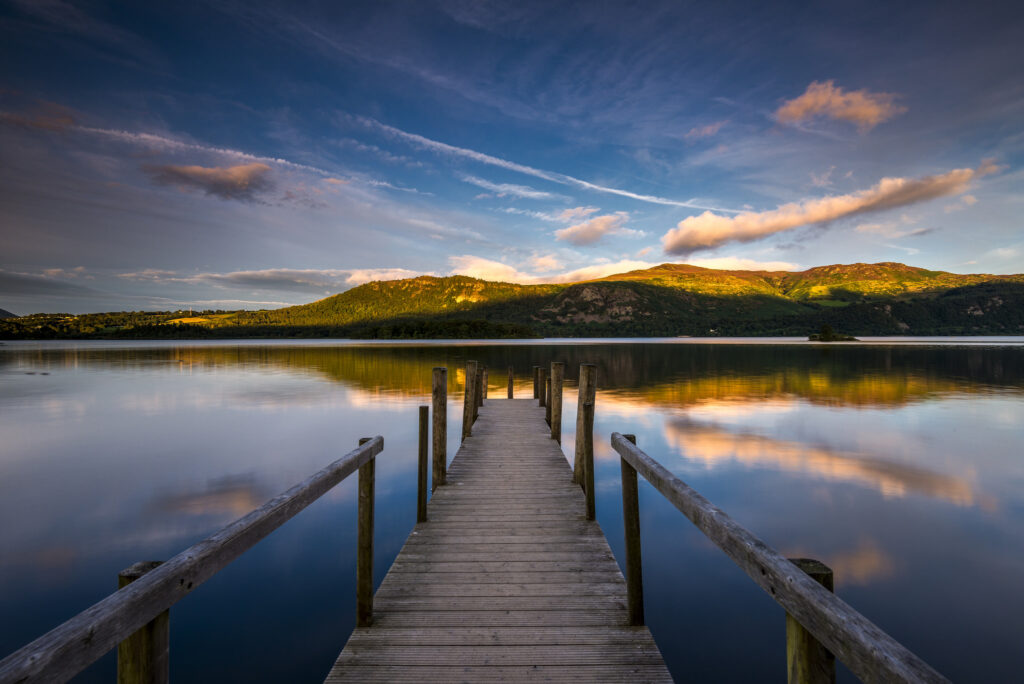 Jetty over Derwentwater on a clear day with a few clouds reflected in water.