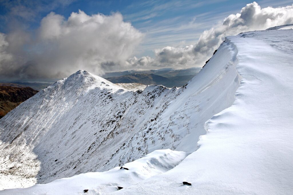 A cornice of snow on the approach to Helvellyn Summit with Swirral Edge and Catstyecam in the background. Lake District Climate