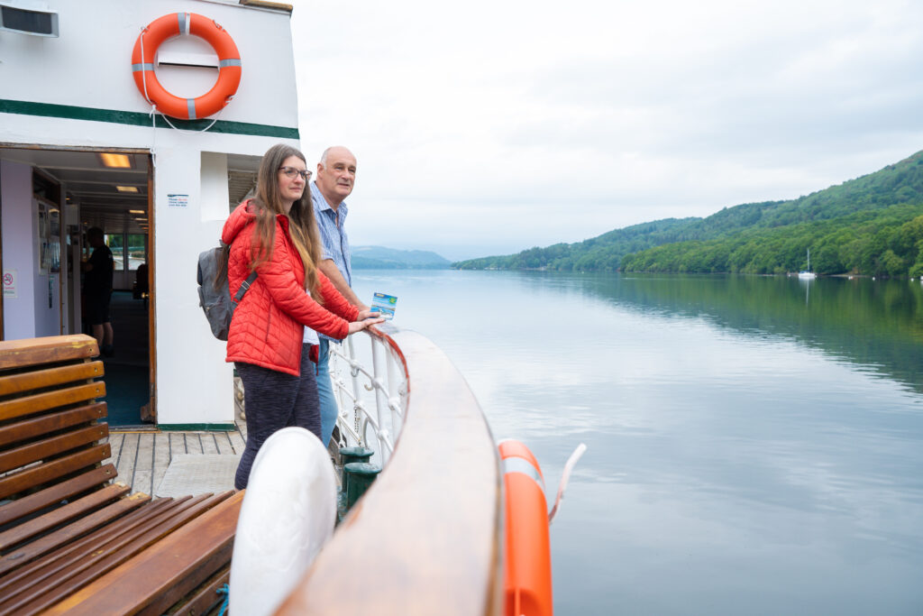 Two people on a Windermere Lakes cruise vessel on Windermere, looking out onto the Lake. Tourism in the Lake District