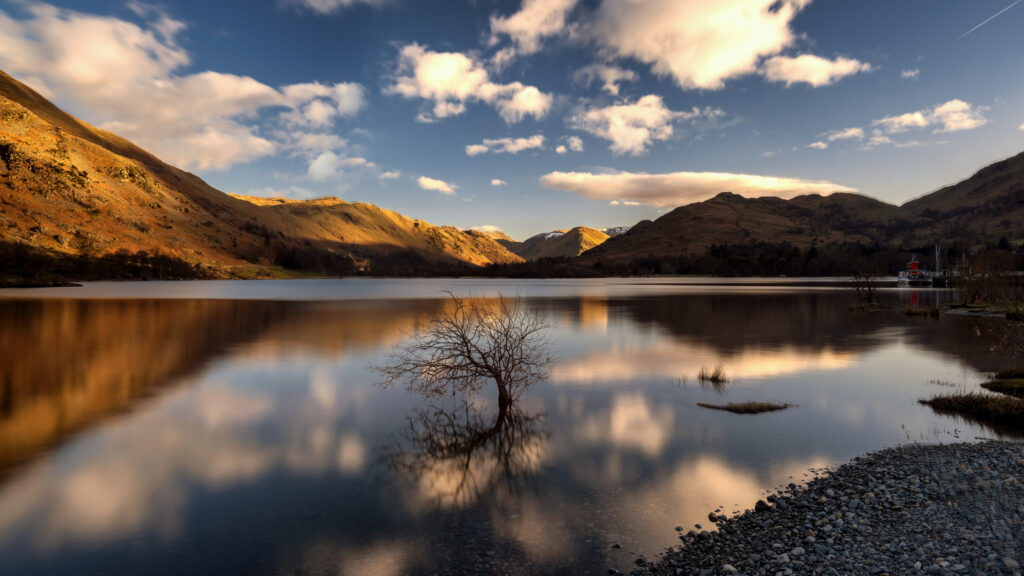 Ullswater at sunset, blue sky with white clouds, orange glowing fells reflected in the water