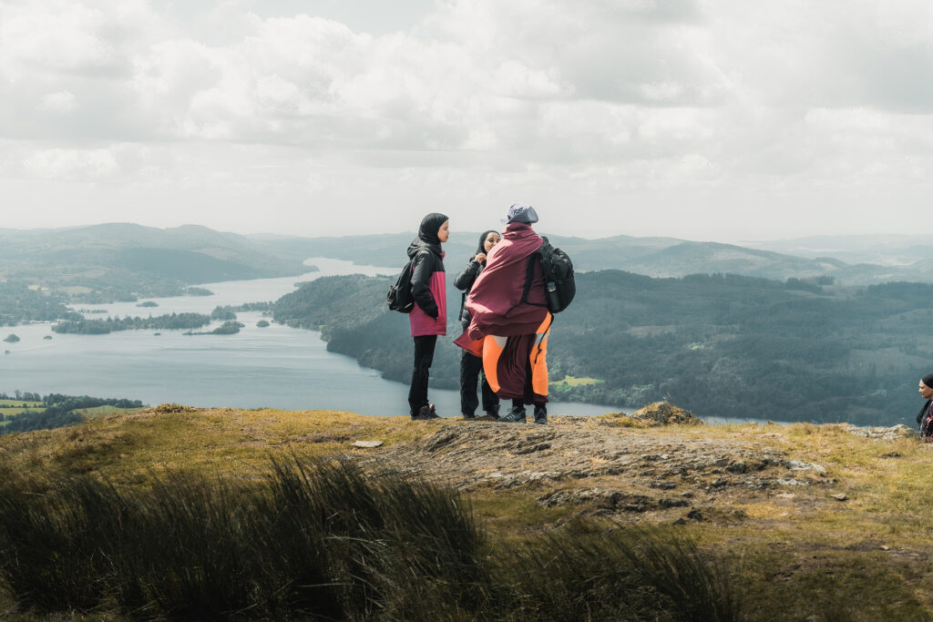 three muslim hikers standing on wansfell pike summit with view of lake and lowland woodland behind