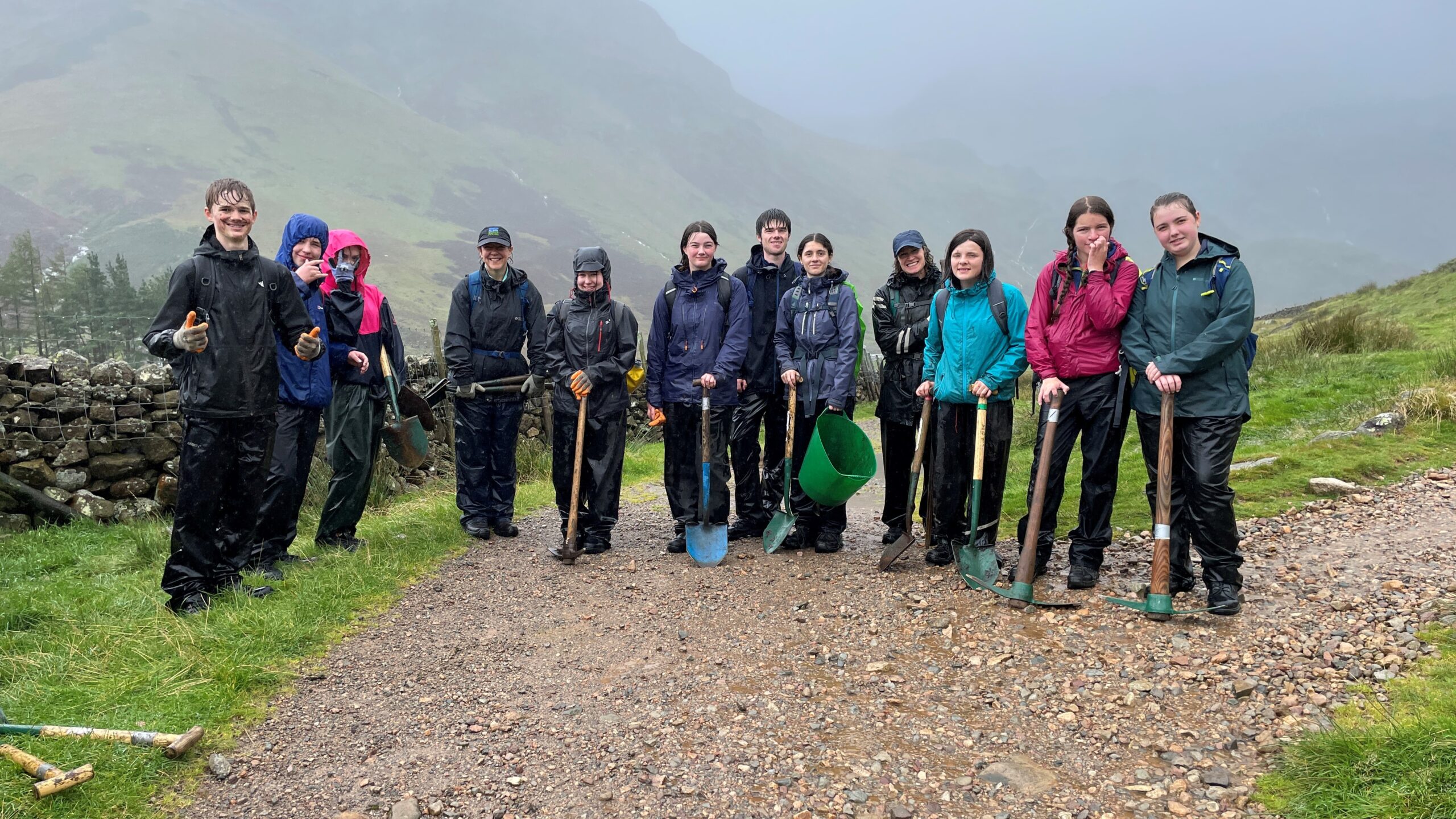 A group of Young rangers in the rain wearing waterproofs and carrying shovels and pick axes. In the Lake District National Park.
