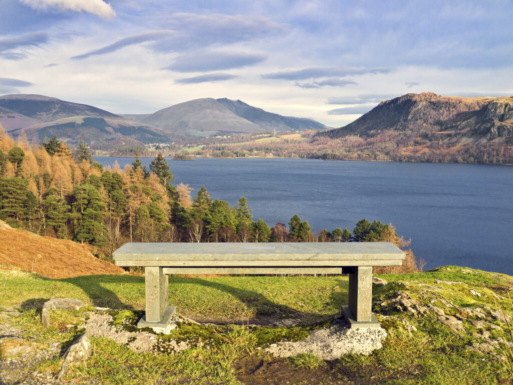 Wooden bench overlooking Derwent Water. woodland and fells on a sunny autumnal day