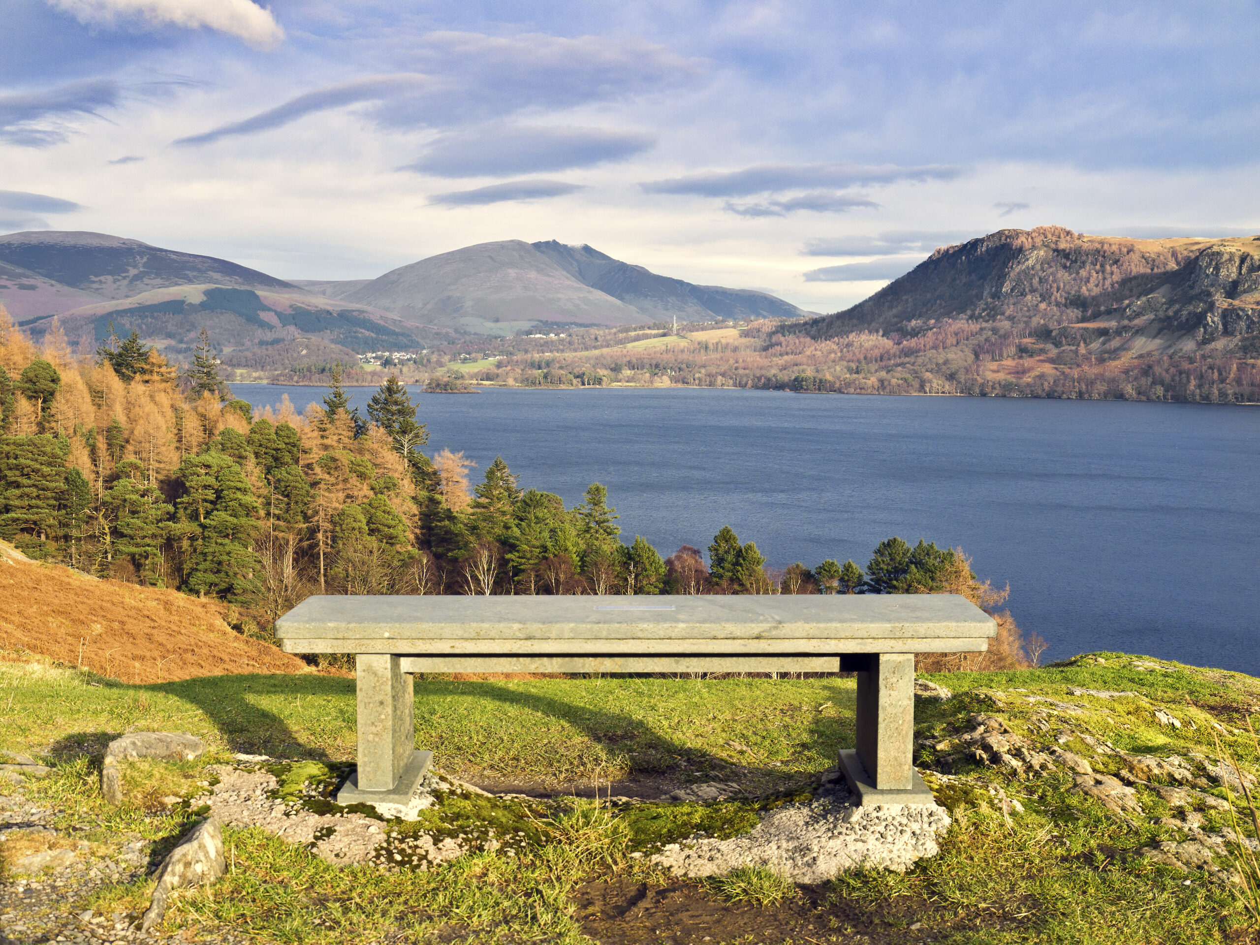 Wooden bench overlooking Derwent Water. woodland and fells on a sunny autumnal day