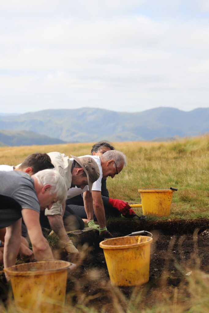 Archaeology volunteers kneeled on floor digging into area