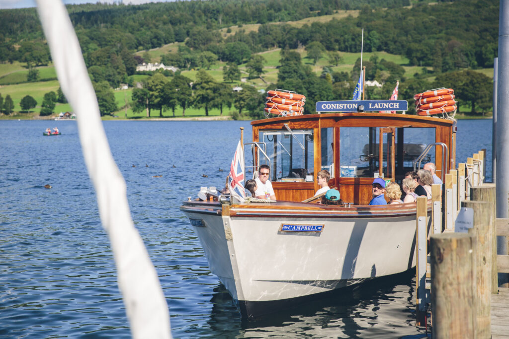 White and wooden motorised boat pulling into wooden jetty on Coniston Water. White rope cuts across bottom left of photo