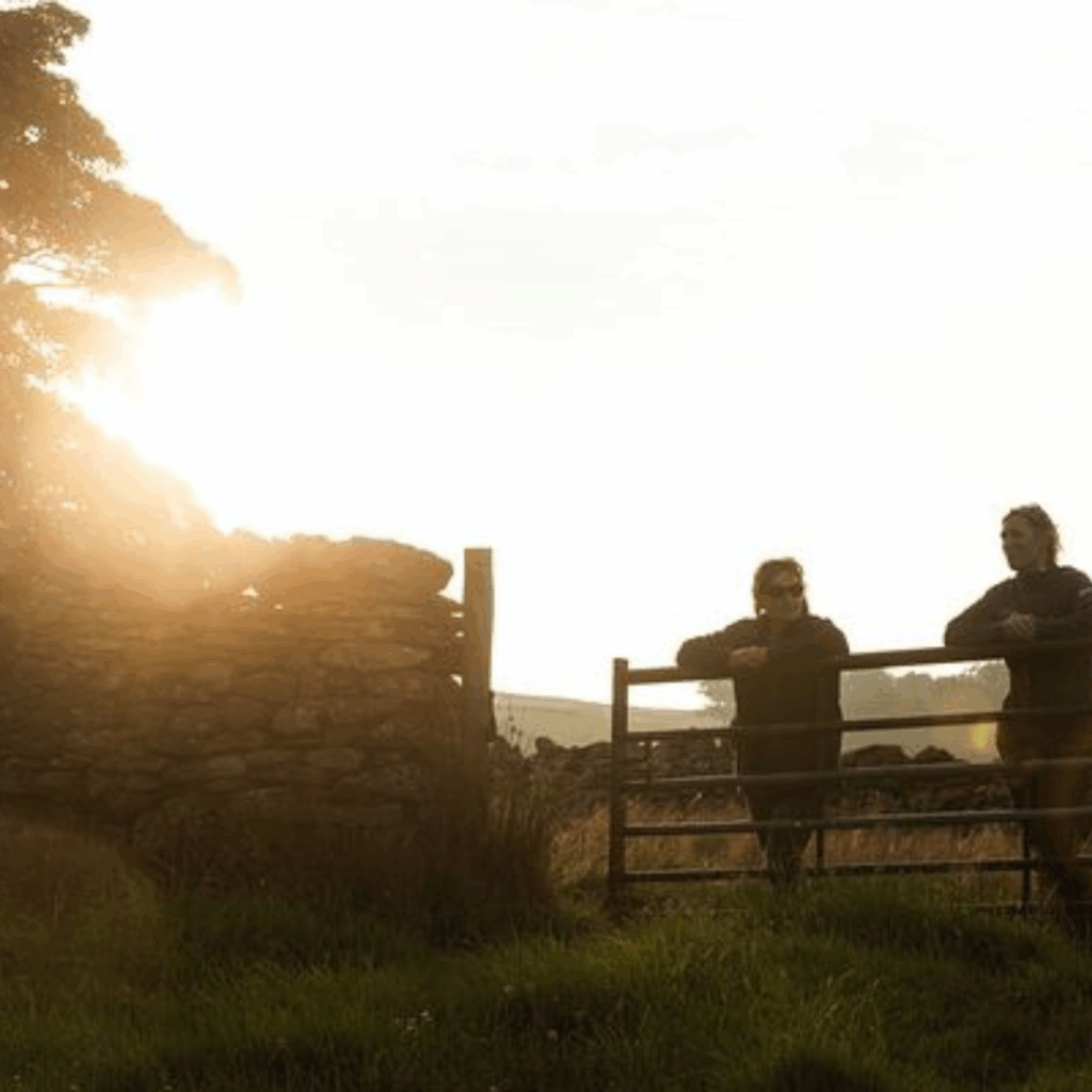 two people stood looking over a gate at sunrise - they're outlined as silhouettes