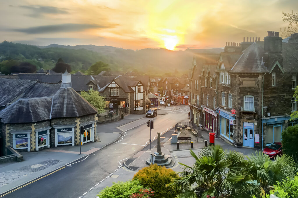 ambleside road lined with shops and gardens at sunset with fells in backdrop