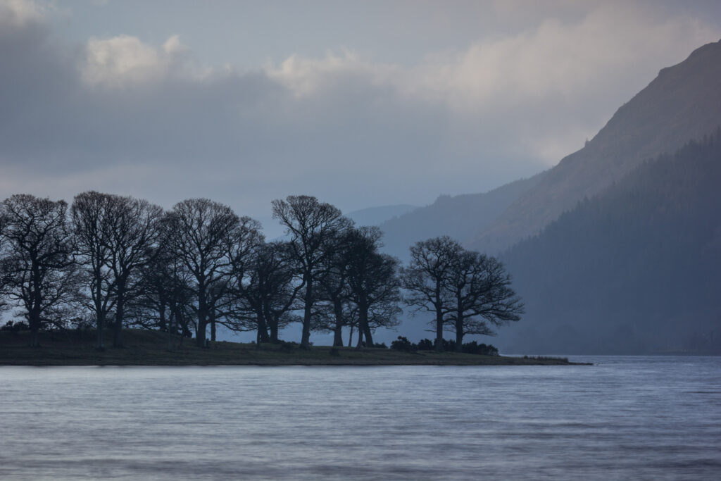 landscape view of Bassenthwaite lake with trees and silhouette of mountains