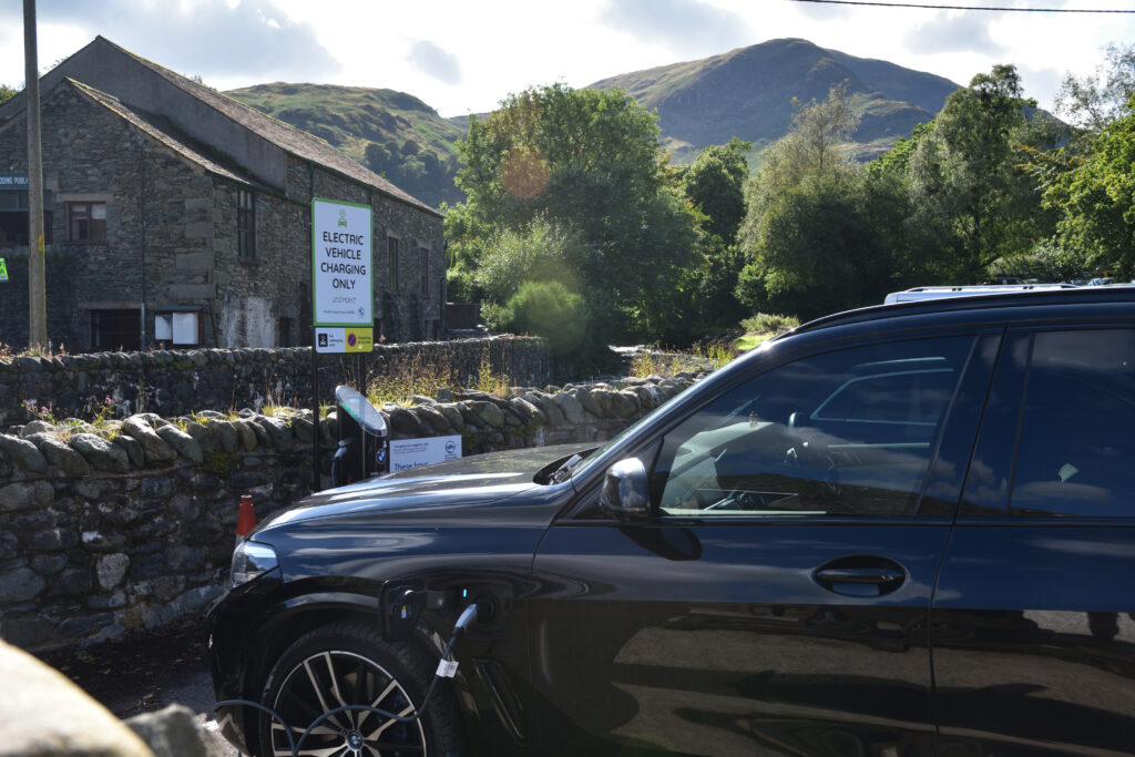 a black car parked up using an EV charger in the Lake District with fells in the background