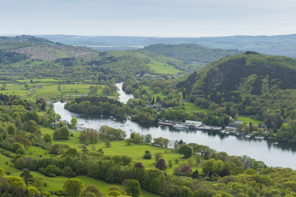 landscape view of fell foot. sunny day, water body surrounded by lush green fields and woodland