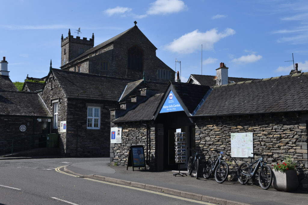 Hawkshead information centre. Grey stone two story building by a road on a blue sky day