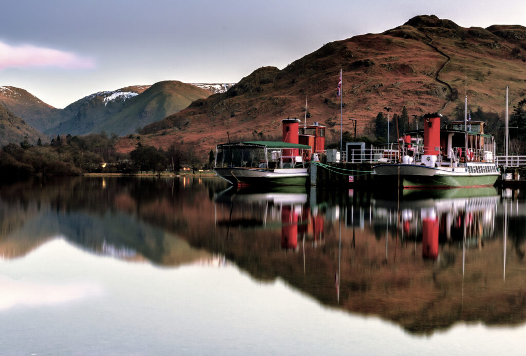 Large boats on Ullswater at sunset, with the fell landscape reflected in the water