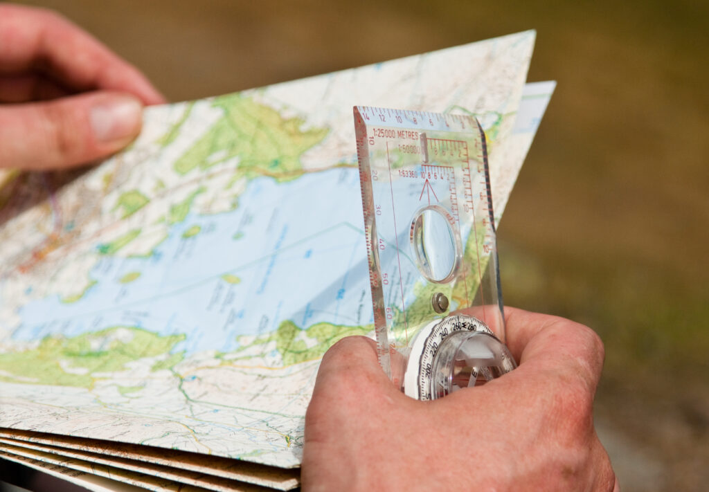 two hands holding folded paper os map and transparent compass