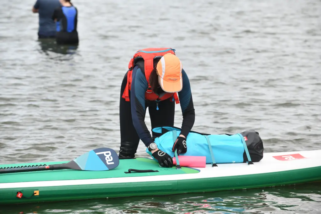 adult stood knee deep in water packing equipment onto turquoise paddle board