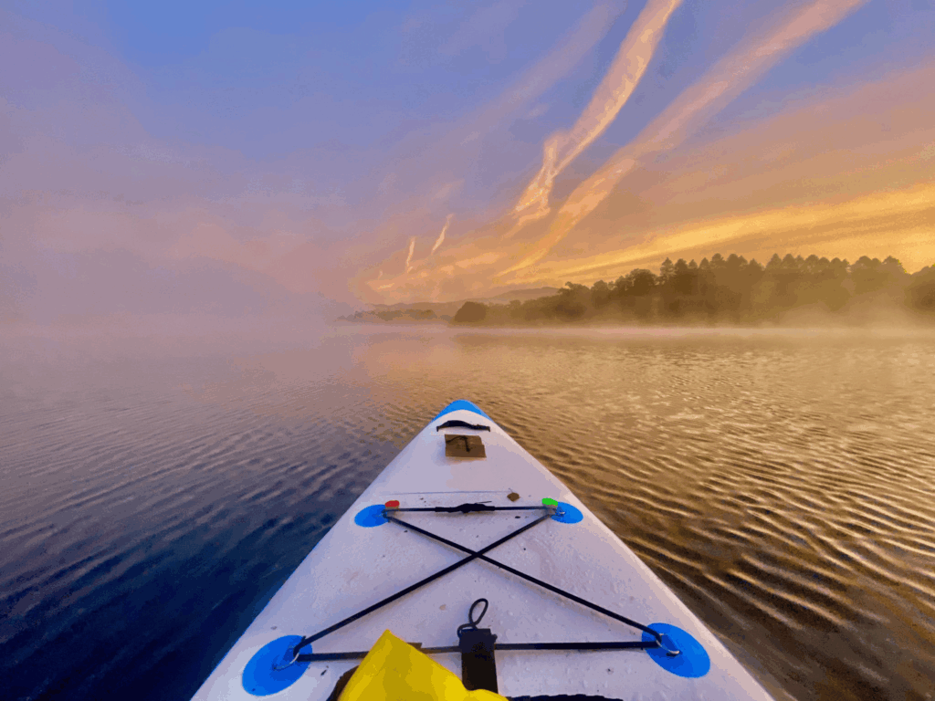 Front of a white paddleboard on a lake at sunset.