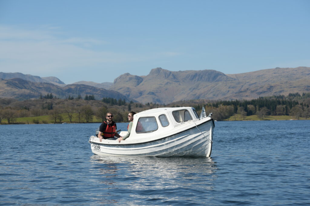 White motor boat with adult male onboard stationary on lake Windermere on a sunny day