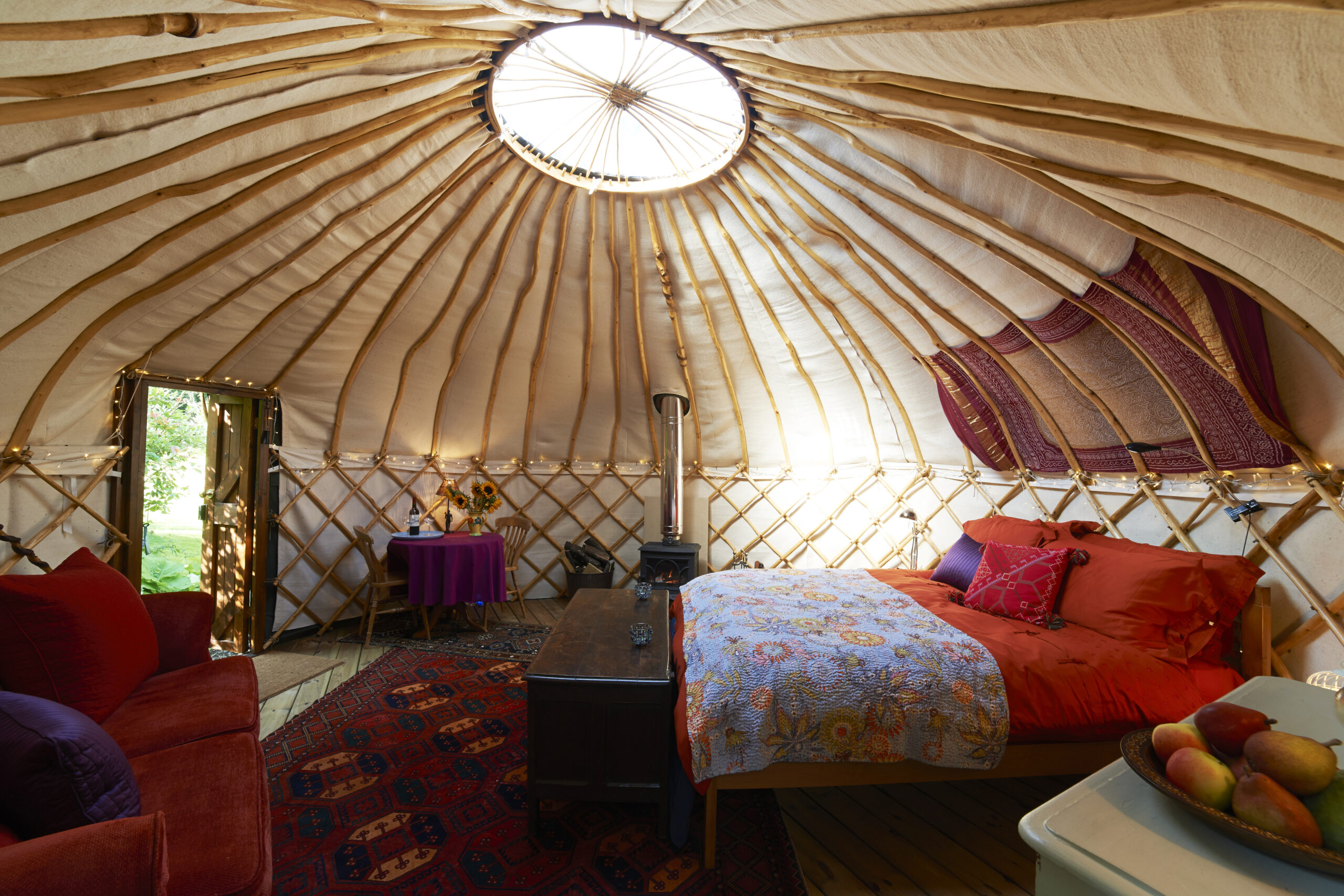 Large circular high ceiling wooden glamping tent, red double bed, red sofa and rug