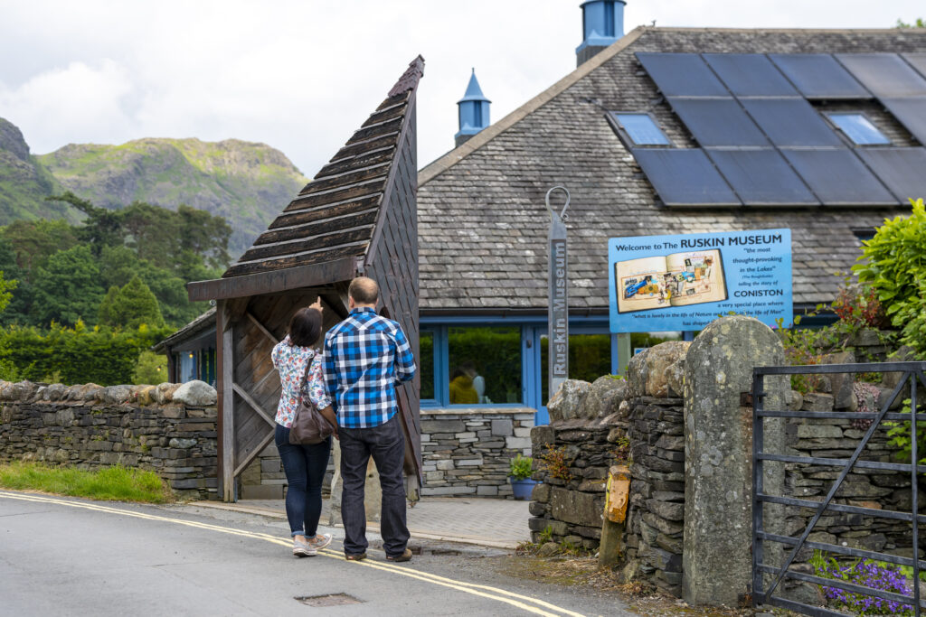 A couple stood outside Ruskin museum in Coniston with mountains behind