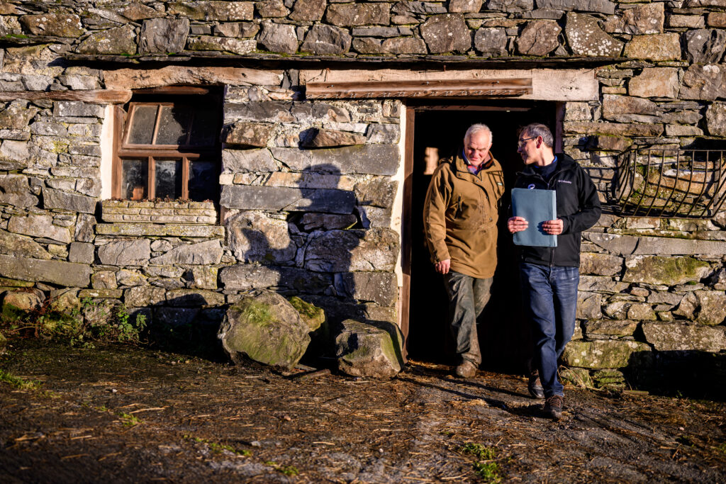 lake district national park planning officer walking out of stone building doorway next to older male farmer