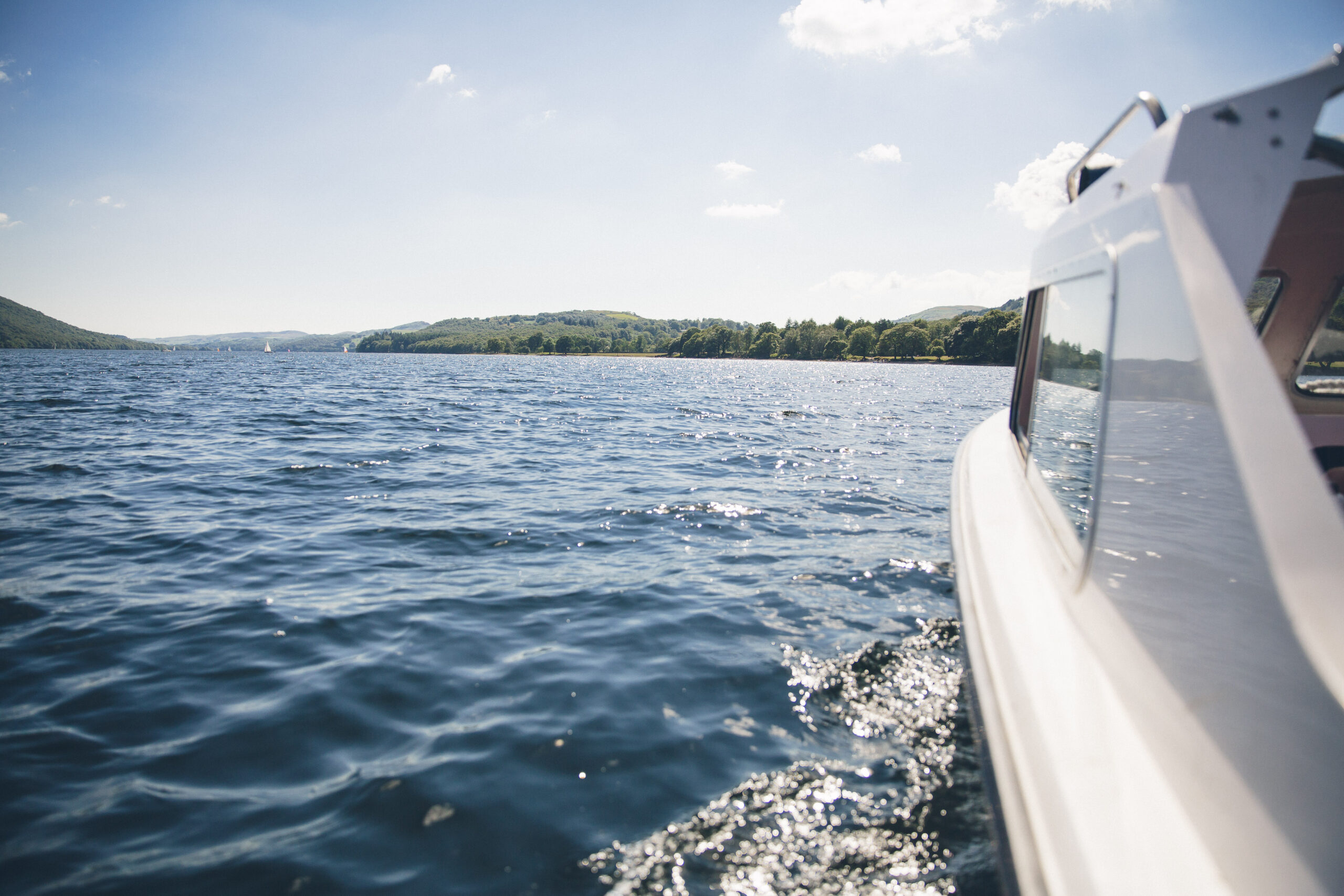 sparkling lake on a sunny day with side of white motorised boat in right of frame